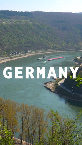 Vertical-Video-Aerial-Drone-Shot-Of-River-With-Cargo-Boats-With-Animated-Graphic-Spelling-Out-Germany